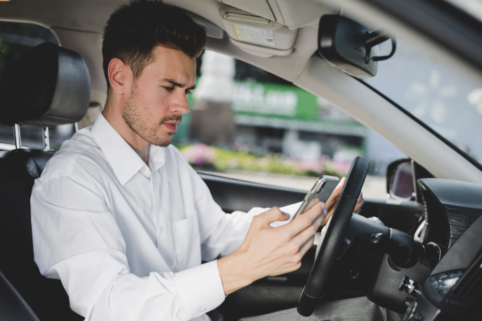 En mann som ser på mobilen sin mens han sitter bak rattet på en bil som står stille